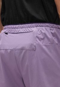 Κοντινό πλάνο ατόμου που φοράει ανοιχτό μωβ παντελόνι με ελαστική μέση και φερμουάρ στην πίσω τσέπη, συνδυασμένο με μαύρο πουκάμισο.