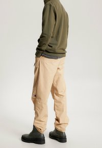 Béžové cargo kalhoty s bočními kapsami, v kombinaci s olivově zelenou mikinou a černými šněrovacími botami, s logem na kalhotách.