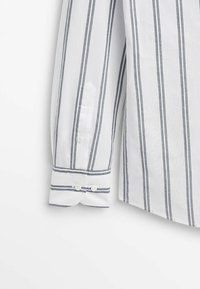 Witte shirt met grijze verticale strepen, met een puntige kraag, enkele knoopmanchet en een contrasterende afwerking aan de rand van de manchet.