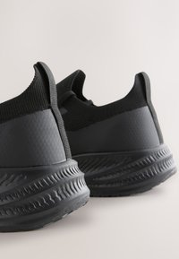 Black athletic sneakers with a textured, flexible upper and a cushioned sole. Design includes a low-profile shape and reinforced heel.