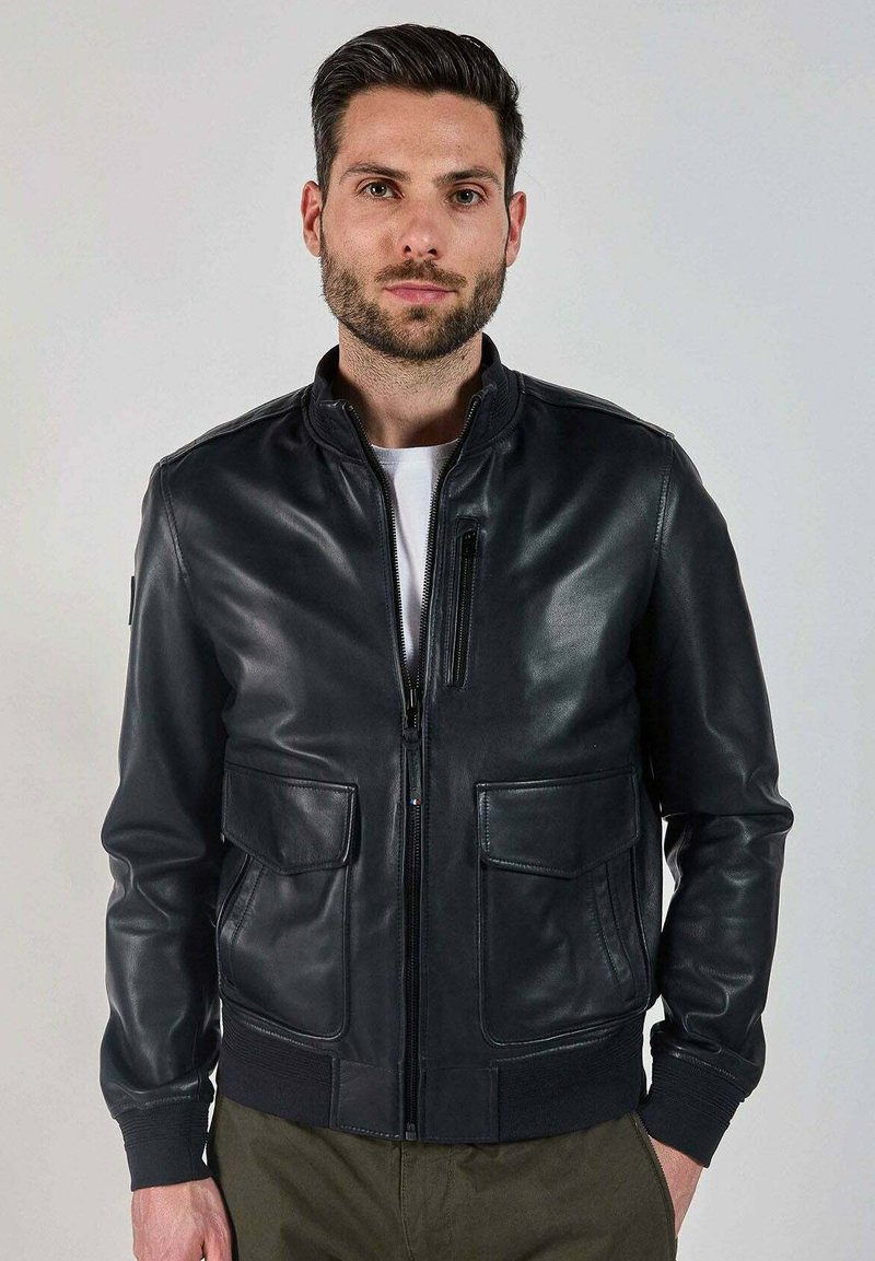 Veste bomber en cuir noir avec col et poignets côtelés, fermeture éclair à l'avant, deux grandes poches à patch et une texture lisse et élégante.