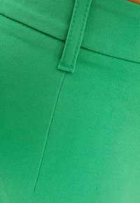 Närbild av grönt tyg med en vertikal söm och en bältesögla sydd i överkanten.