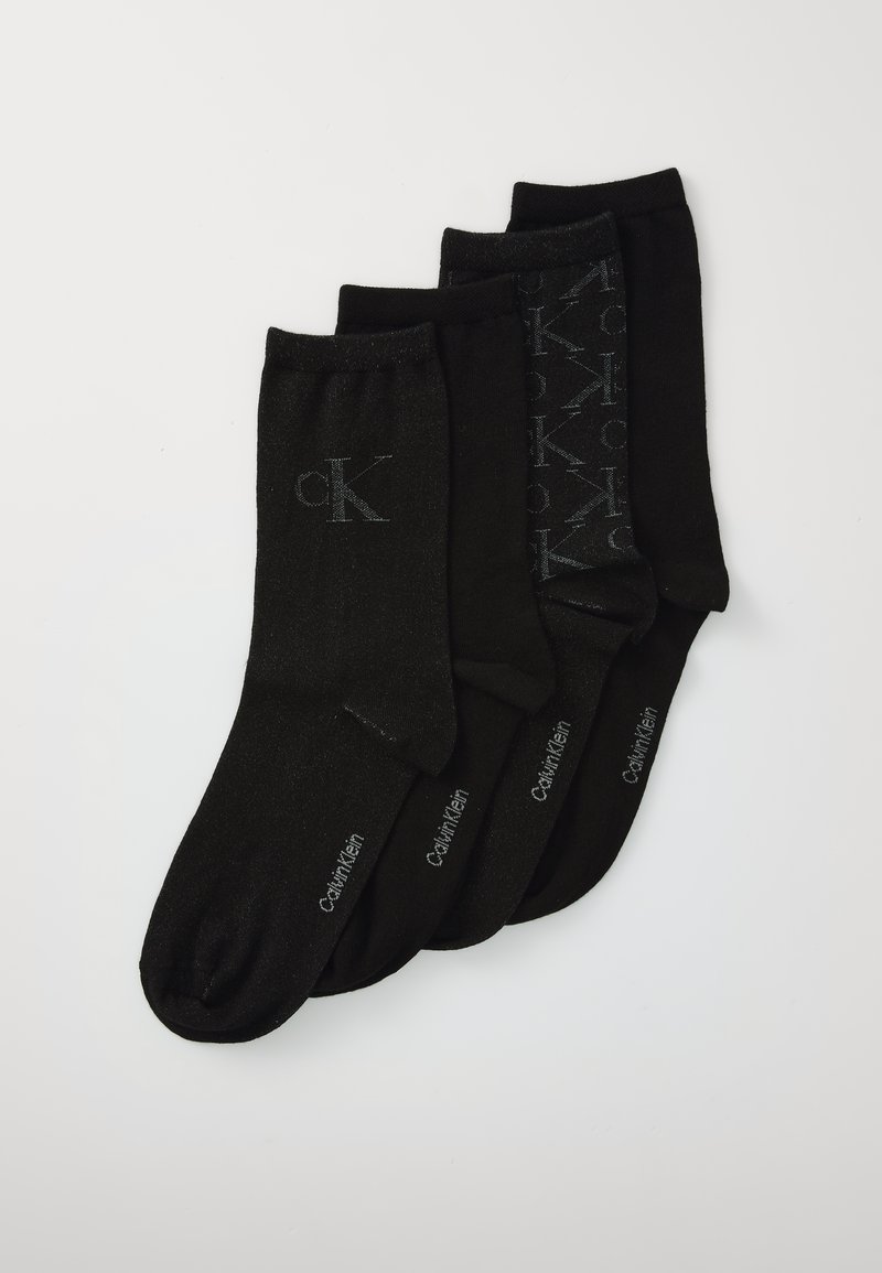 Četri pāri melnu Calvin Klein zeķu, sakārtoti pārklājoši, ar logotipa iniciāļiem un zīmola nosaukumu uz katra pāra.