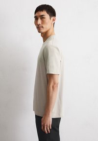 Lichtbeige t-shirt met korte mouwen en een ronde halslijn; gladde textuur; heeft een relaxte pasvorm; gedragen met donkere broeken; eenvoudig ontwerp.
