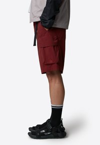Red cargo shorts with side pockets, paired with black sandals and striped black socks. The shorts feature a logo detail on the hem.