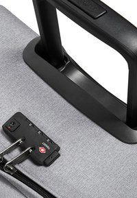 Grå stoffkuffert med et sort teleskophåndtag. Har en kombinationslås og lynlåse for sikker lukning. Tekstureret materiale finish.