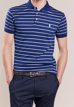 Polo rayé bleu et blanc avec un col et une patte de boutonnage à trois boutons, associé à un pantalon bleu marine et une ceinture tissée marron.