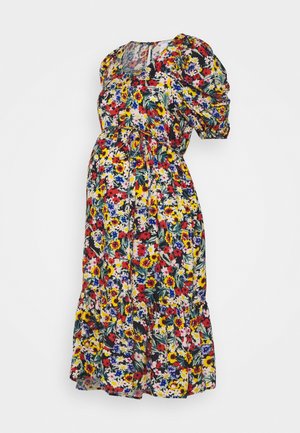 Robe de maternité florale avec manches courtes bouffantes, taille ajustée avec un lien, et jupe fluide aux motifs multicolores rouges, jaunes et bleus.