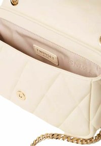 Borsa trapuntata color crema con accessori dorati, tracolla a catena e fodera interna con etichetta del marchio. Chiusura con bottone a pressione circolare.