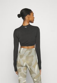 Top corto negro de manga larga con cuello alto y logo blanco. Combinado con leggins de cintura alta que presentan un patrón floral abstracto en tonos beige y marrón.