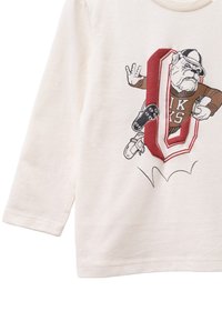 Cremfarbendes Langarmshirt mit einem Cartoon-Bulldog-Motiv in Braun, Rot und Schwarz, das einen Gaming-Controller und Sportelemente zeigt.