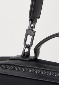 Sac en tissu noir avec une finition mate, des accents en cuir et du matériel en métal brillant. Comprend une fermeture éclair et une bandoulière détachable avec un clip.