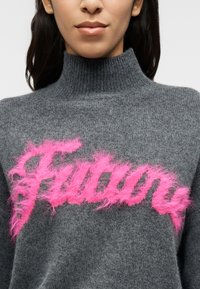 Γκρι πουλόβερ ζιβάγκο από απαλό ύφασμα με ένα χνουδωτό ροζ λογότυπο «Future» στην μπροστινή πλευρά, τονίζοντας την υφή και την αντίθεση.