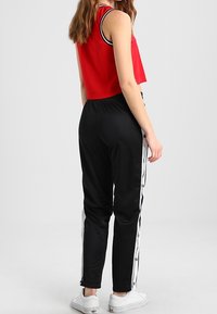 Röd ärmlös crop top matchad med svarta joggers med vita sidoknappar och ränder, kompletterad med vita sneakers.