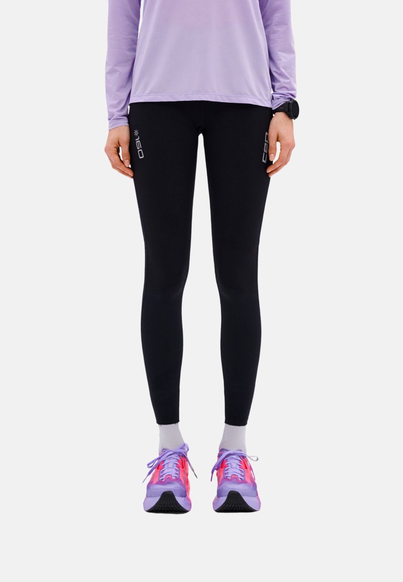 Person wearing black compression leggings with "160" text, light purple long-sleeve top, white socks, and purple-pink running shoes, standing still.