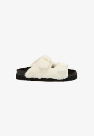 Sandale slide blanche en peluche avec deux brides ajustables, semelle noire, et une finition douce et texturée. Design plat pour le confort.
