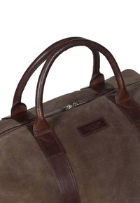 Sac de voyage en cuir brun et daim avec des poignées arrondies doubles, une fermeture zippée et une forme rectangulaire. Présente une étiquette 'Howard'.