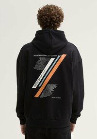 Zwarte hoodie met een grote grafische afbeelding op de achterkant, voorzien van diagonale strepen in oranje, blauw en wit, naast tekst in een vetgedrukt lettertype.