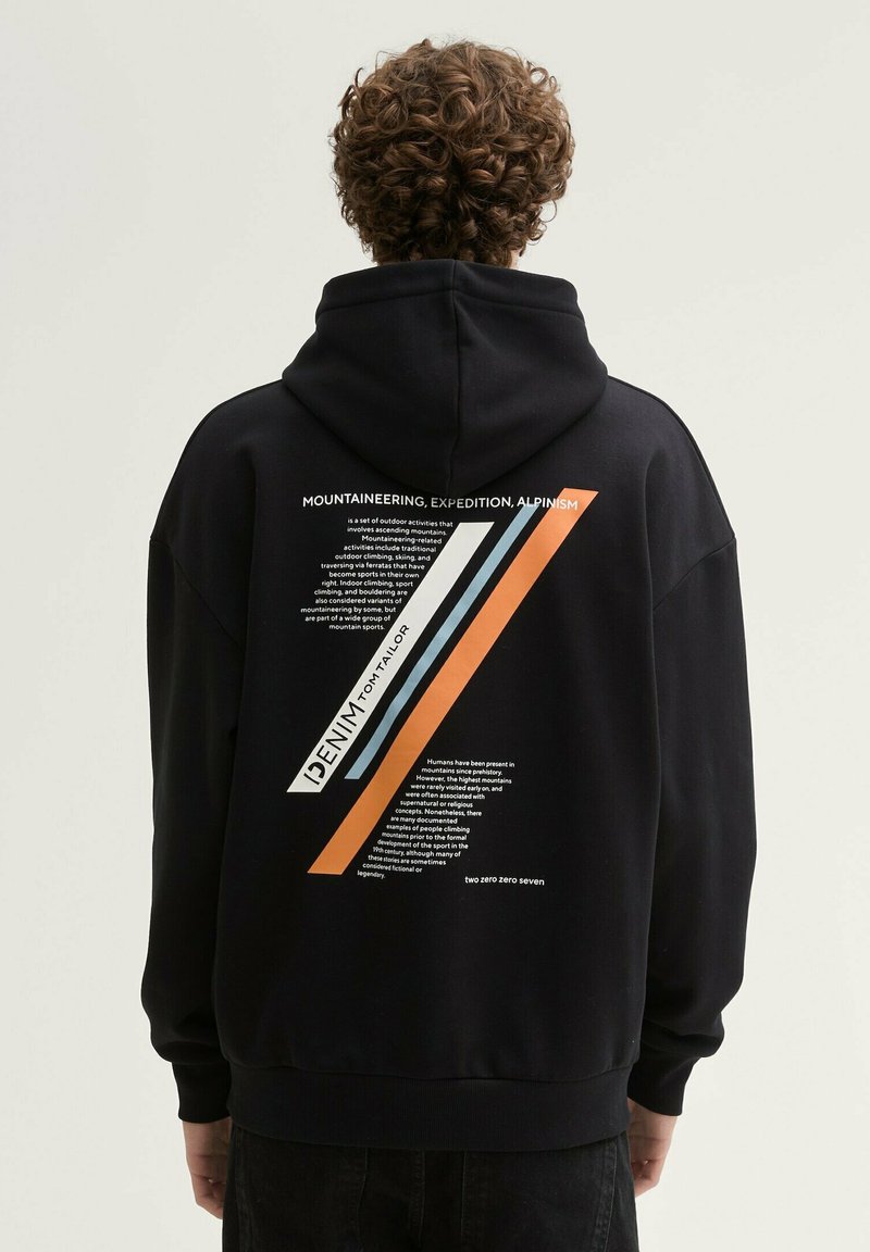 Zwarte hoodie met een grote grafische afbeelding op de achterkant, voorzien van diagonale strepen in oranje, blauw en wit, naast tekst in een vetgedrukt lettertype.