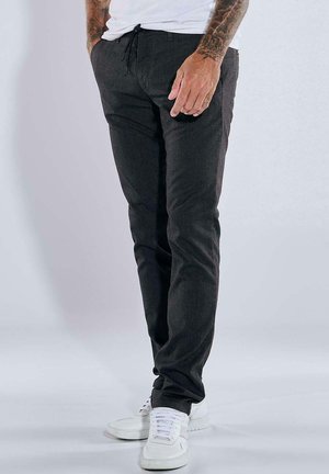 Dark gray pants made of a textured fabric, featuring a drawstring waist and slim fit, paired with white athletic shoes.