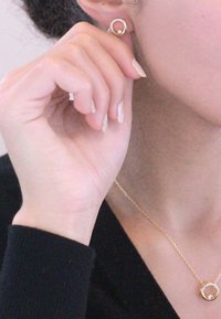 Orecchini d'oro con design circolare piccolo, impreziositi da cristalli. Una delicata collana d'oro presenta un pendente circolare coordinato.