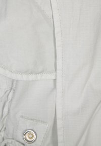 Jasnoszara tkanina z wzorem kratki, z guzikiem z złotym akcentem oraz haftowaną kieszenią. Teksturowana powierzchnia, casualowy design.