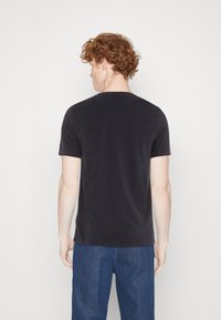 Sort kortærmet t-shirt lavet af bomuld, med en klassisk rund hals og en almindelig pasform, vist fra ryggen mod en ensfarvet baggrund.