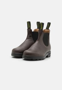 Bottes Chelsea en cuir marron avec panneaux latéraux en élastique, semelles en caoutchouc noir et languettes vertes. Texture lisse et design à bout rond.