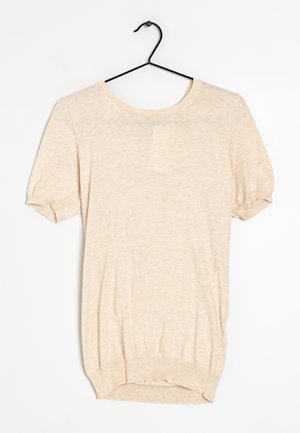 Haut en maille beige à manches courtes avec encolure ronde et poignets côtelés, suspendu sur un cintre noir sur fond blanc.