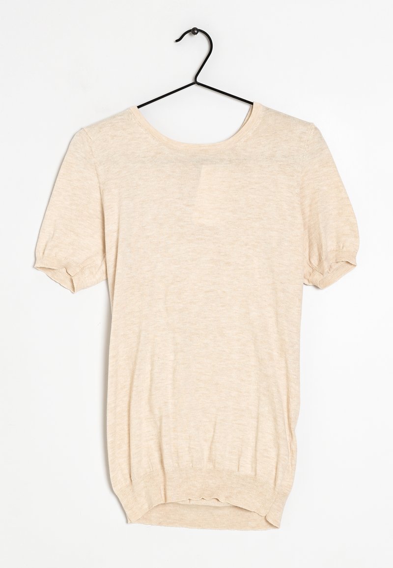 Haut en maille beige à manches courtes avec encolure ronde et poignets côtelés, suspendu sur un cintre noir sur fond blanc.