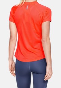 Röd idrottströja med korta ärmar, med en strukturerad tyg och reflekterande detaljer bak. Matchas med blå leggings.