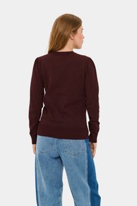 Ciemnobordowy sweter z długimi rękawami, ściągaczami na mankietach i dole, w połączeniu z jasnoniebieskimi spodniami z szerokimi nogawkami. Sweter ma delikatne bufiaste ramiona.