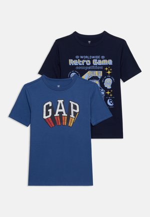 Δύο κοντομάνικα t-shirts με στρογγυλή λαιμόκοψη· ένα μπλε με το "GAP" σε ρετρό στυλ και ένα μαύρο με πολύχρωμο γραφικό από arcade παιχνίδι και την επιγραφή "Retro Game".