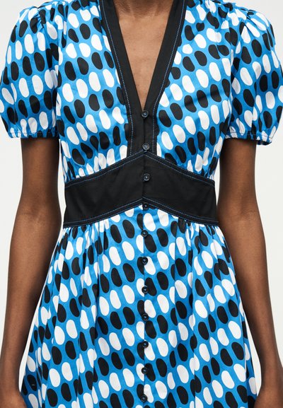 Μπλε φόρεμα με μαύρο και λευκό οβάλ σχέδιο, μαύρα κουμπιά στο μπροστινό μέρος, κοντά φουσκωτά μανίκια και μαύρη ζώνη στη μέση με μπλε ραφές.
