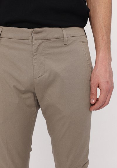 Beige bomullsbukser har en smal passform med platt front, sidofickor och en slät textur, tillsammans med en svart skjorta.