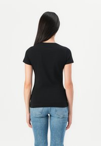 Black short-sleeve t-shirt with a classic crew neck, made of smooth cotton fabric. Paired with light blue denim jeans.