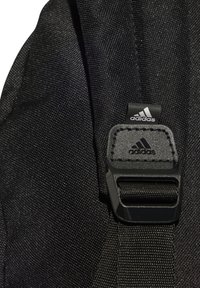 Spallaccio di zaino in tessuto nero con una fibbia in plastica con il logo Adidas in rilievo e dettagli cuciti, che mostra un motivo di tessitura testurizzata.