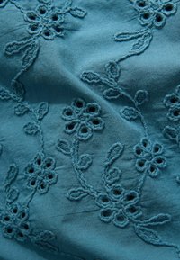 Tessuto teal con intricato ricamo floreale, dettagli intagliati e viti che si intrecciano. Texture morbida e motivi floreali distintivi.