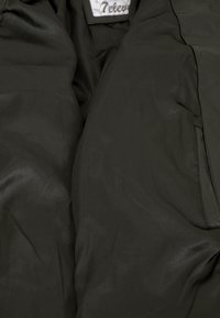 Schwarze gepolsterte Jacke mit Innenfutter aus glattem, leichtem Stoff mit dezentem Glanz. Enthält ein Etikett am Hals.