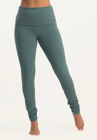 Hochgeschnittene, türkisfarbene Leggings aus dehnbarem Stoff. Mit einem umschlagbaren Bund und Raffung an den Knöcheln. Glatte Textur.