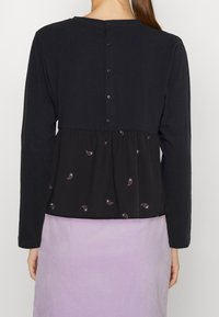 Svart långärmad topp med en rynkad nederdel med lila paisleymönster, rundad halsringning och knappstängning bak.