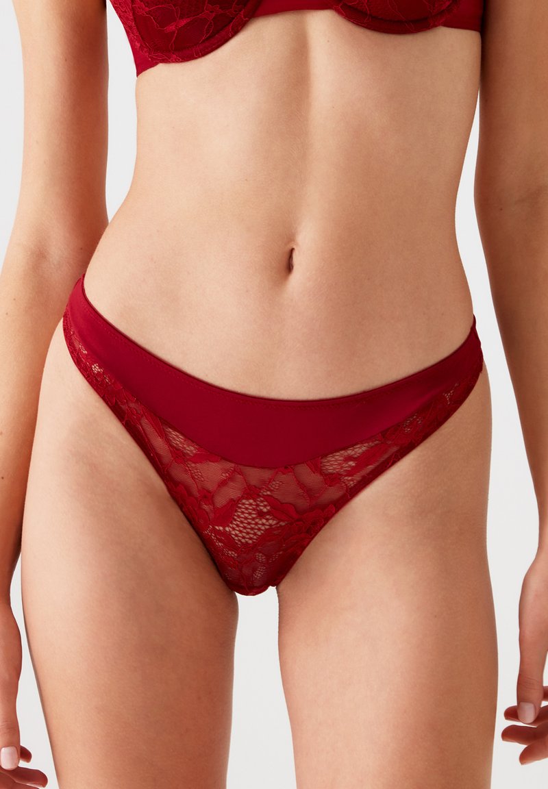 Rode lingeriestring met een kanten inzet en een gladde tailleband. De kant heeft bloemmotieven, contrasterende texturen en een lage fit.