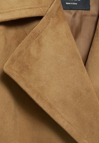 Tissu en daim marron avec une texture lisse ; possède un large revers et une doublure intérieure visible, mettant en valeur une couleur beige chaud.