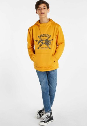 Felpa gialla con stampa grafica nera, caratterizzata da motivi di sci. Abbinata a jeans blu e sneakers nere, crea un look casual.