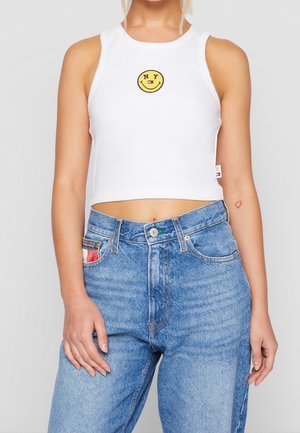 Witte cropped tanktop met een gele smiley face-logo en "NY" tekst, gecombineerd met hoog-geknipte blauwe denim jeans met een patch pocket.