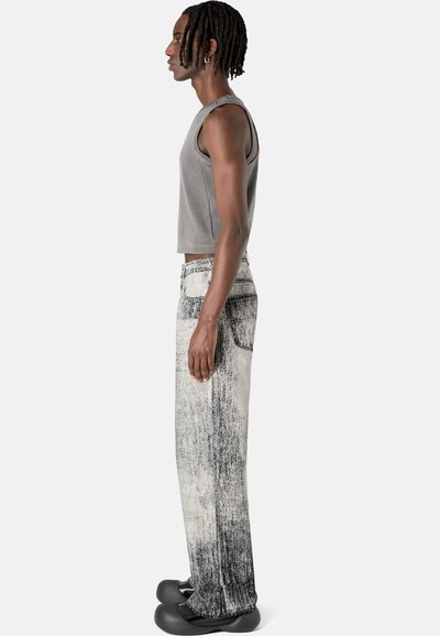 Gray cropped tank top paired with high-waisted denim jeans featuring a black and white distressed pattern, worn with black footwear.