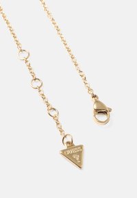 Gouden ketting met een driehoekige hanger met het "GUESS"-logo en een karabijnsluiting voor het sluiten. Gladde en glanzende afwerking.