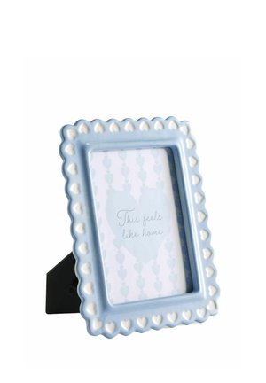 Blue photo frame with white heart designs on the border, standing on a black easel, holding paper with "This feels like home" text.