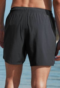 Schwarze Schwimmshorts aus glattem Stoff mit einem elastischen Bund, der einen lockeren Sitz und Seitenschlitze für eine optimale Bewegungsfreiheit bietet.