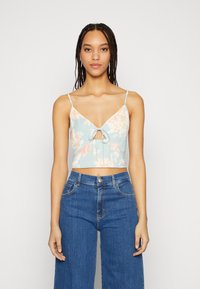Top cropped floral em azul claro com flores em rosa-laranja, alças spaghetti e um laço na parte da frente. Combinado com jeans azuis de cintura alta.